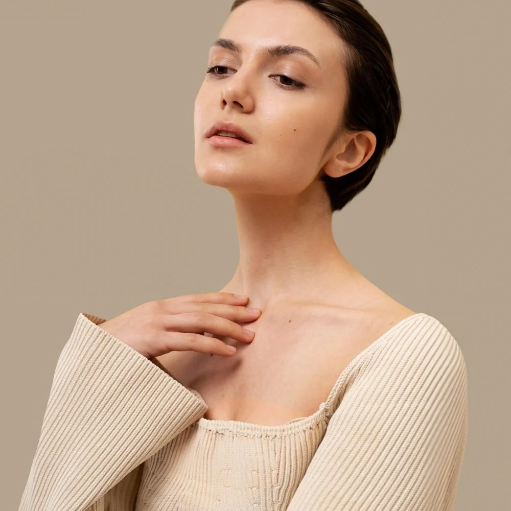Woman in beige sweater posing thoughtfully